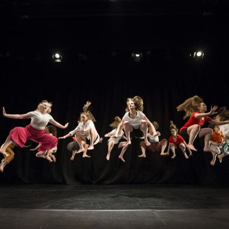 14 dancers in t-shirts and trousers seemingly hover in the air.