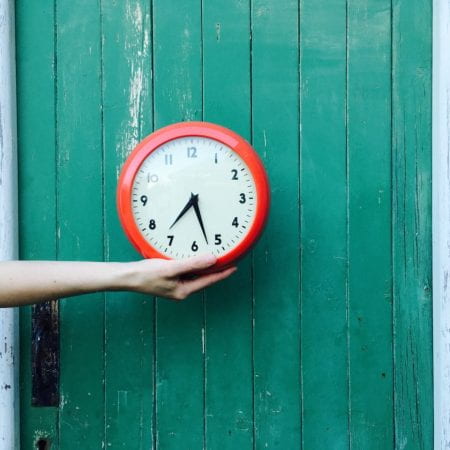 An outstretched hand holds a red and white wall clock.