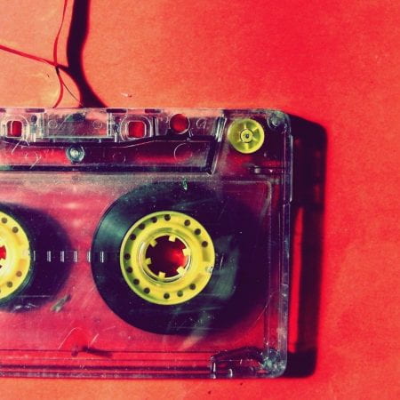 An unspooled C90 cassette tape lying on a red background.