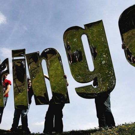 Large mirrors in the shape of letters (spelling FRINGE) held against a blue sky.