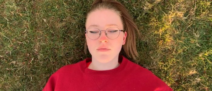 A young woman in a red sweatshirt lays on the grass with her eyes closed.